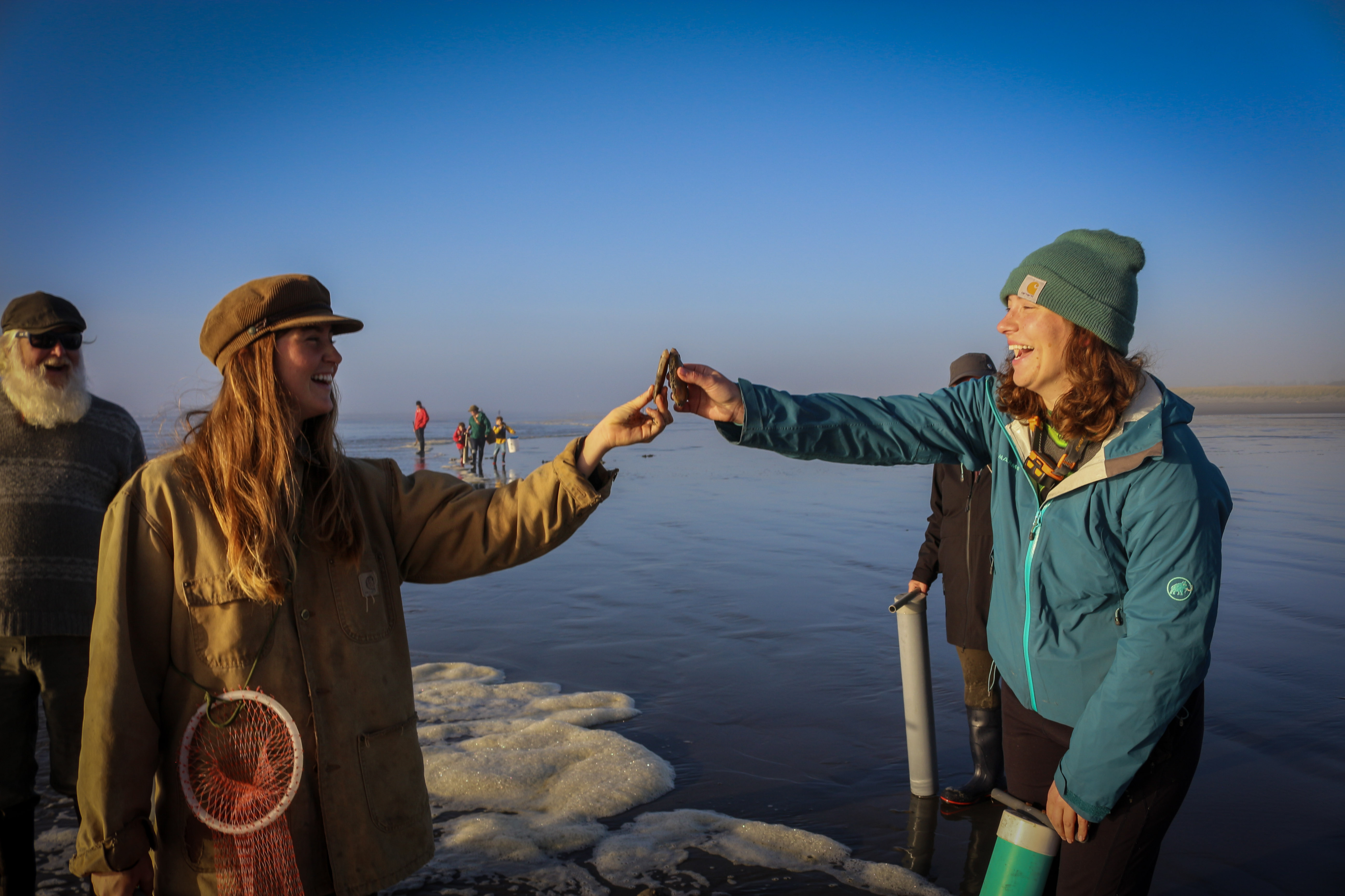Two people posing as though they are toasting champagne; only instead of glasses, they are holding razor clams.